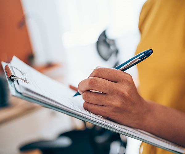 Person writing on clipboard with a pen