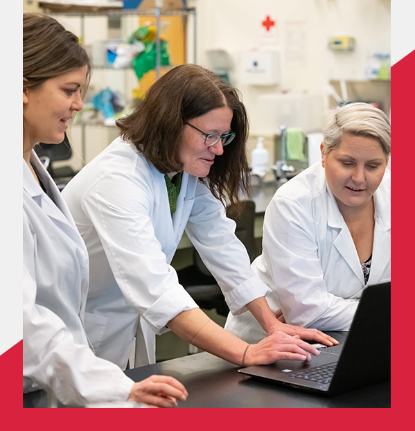 Teacher and two students on a laptop wearing lab coats in classroom