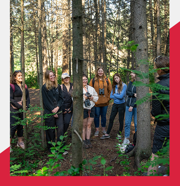 students standing in a forest listening to an instructor speaking