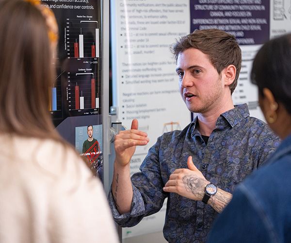 student speaking to other students in front of his display at Student Research Day