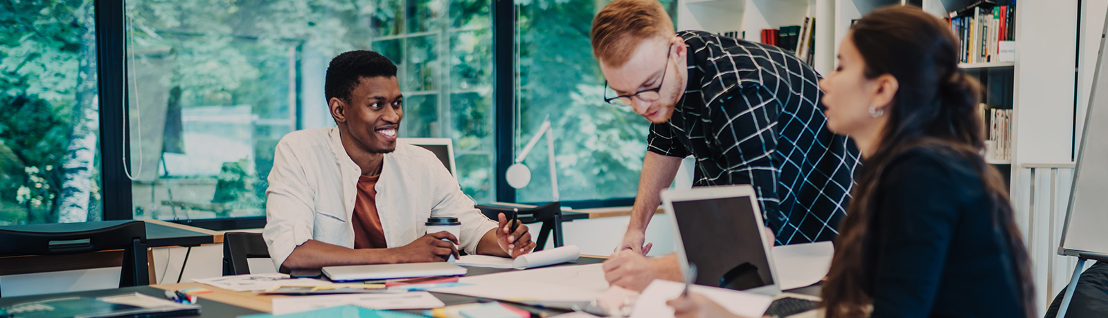 A diverse group of professionals collaborating on a project in a modern office setting, representing MacEwan University's School of Continuing Education AI & Innovation Training