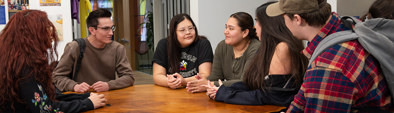 Students sitting together around a table at kihêw waciston, talking and smiling.