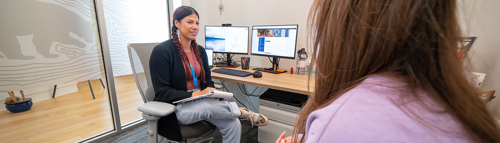An Indigenous student advisor smiles while meeting with a student in a kihêw waciston office