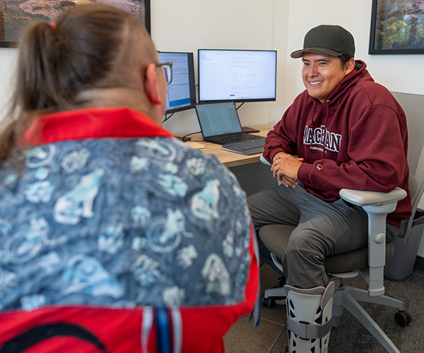 An advisor wearing a MacEwan University hoodie speaks with a student in a kihêw waciston office.