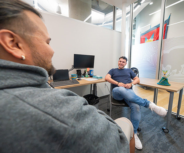 A Knowledge Keeper and a student sit cross-legged on a rug in kihêw waciston