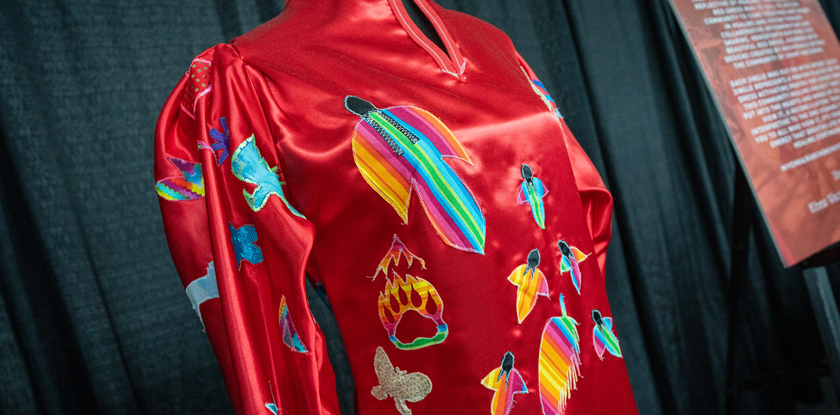 A red satin dress embroidered with colourful feathers, animals, and symbols
