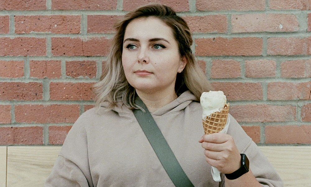 Kelsey Friesan stands outside in front of a red brick wall, holding an ice cream cone.
