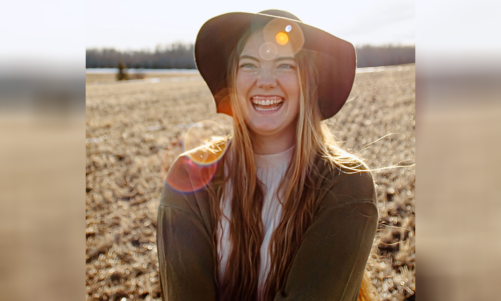 Dana McGonigal stands outside in a field wearing a large-brimmed hat and a big smile.