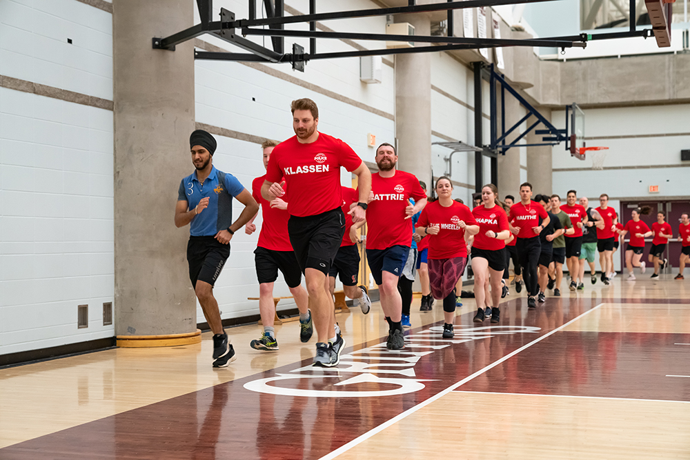 A group of students wearing red t-shirts run in a line through a gymnasium.