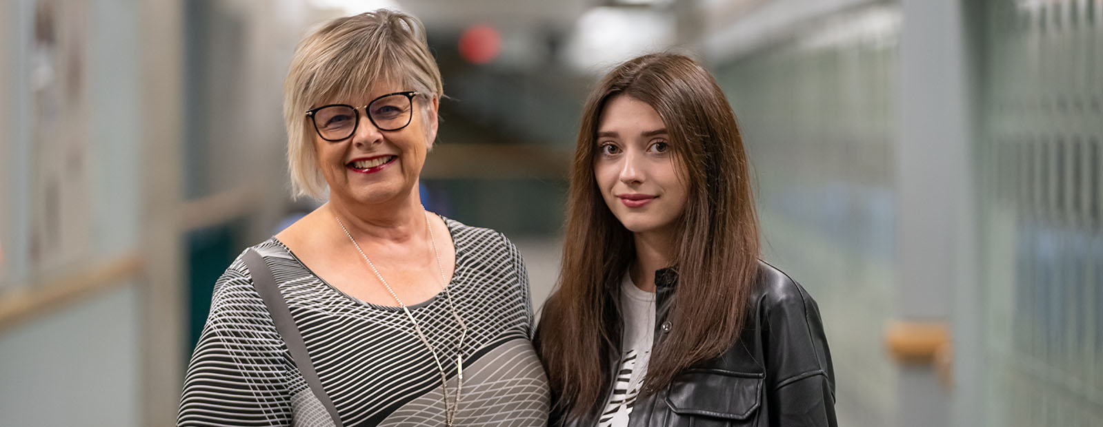 Instructor Melody Kostiuk and student Anna Berovan stand together in a hallway in MacEwan's Building 6.