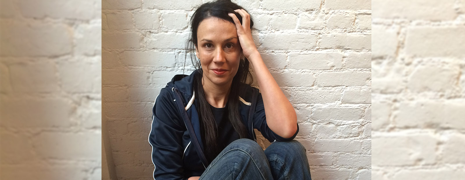 Author Rivka Galchen sits against a white brick wall