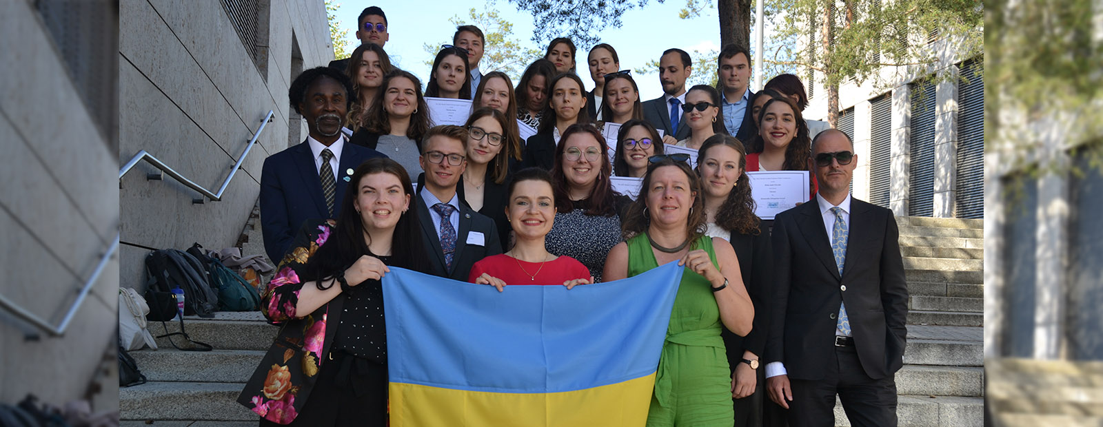 A group of faculty and students gather on a set of stairs with a Ukrainian flag