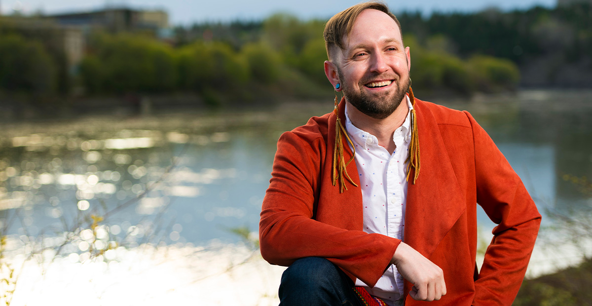 Keith King sits on a lakeshore, smiling.