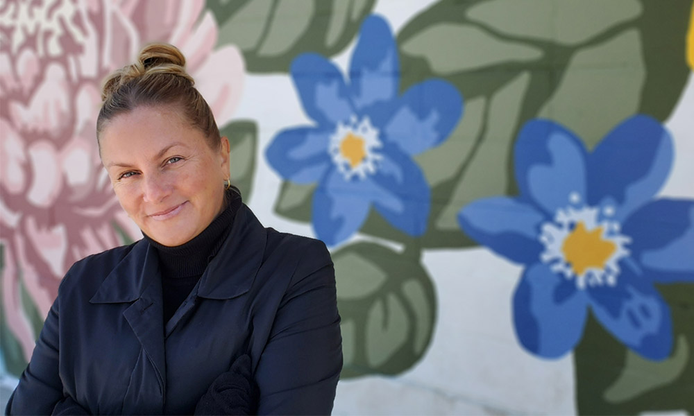 Joni smiling in front of a mural with large painted blue and pink flowers