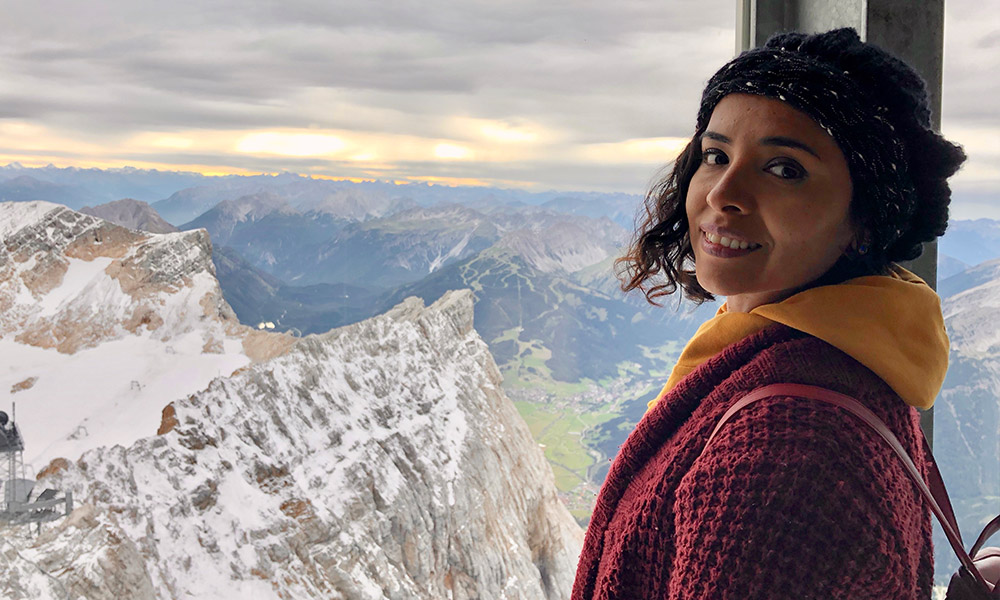 Lia standing in front of a window overlooking a snowy mountain range