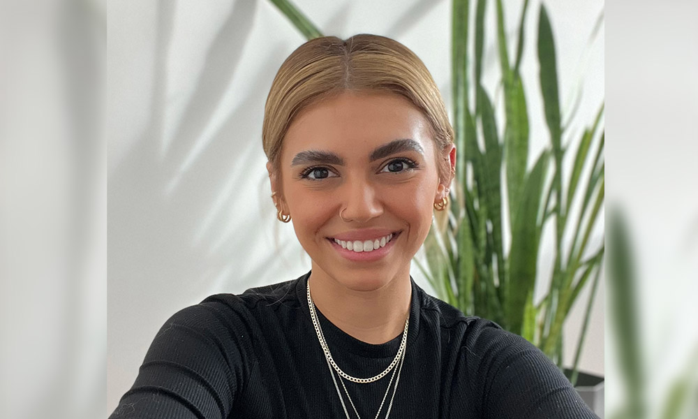 Headshot of Natasja Pitcher in front of a tall green plant and white wall.