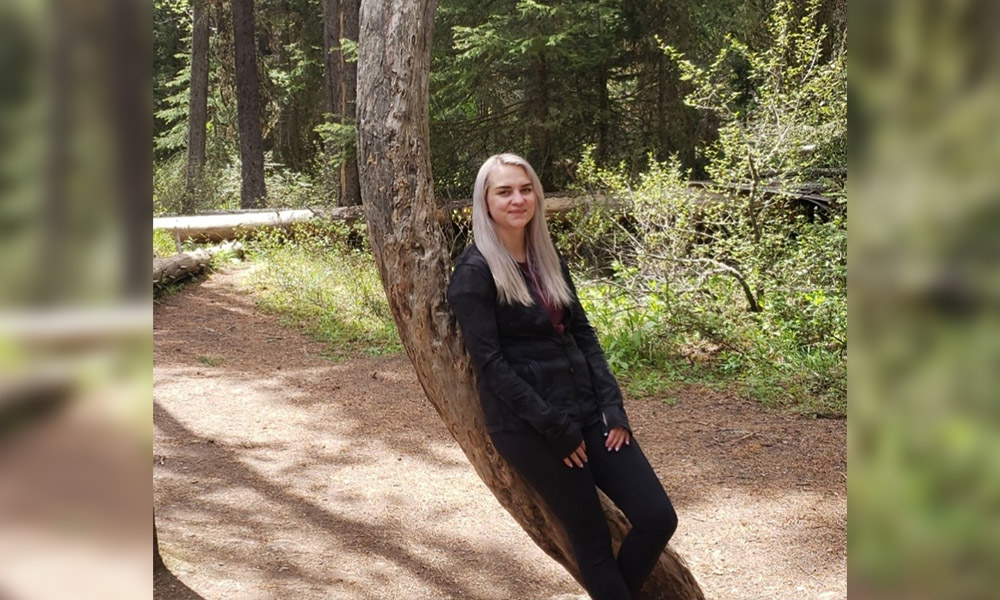 Samantha leaning against a bending tree beside a gravel path