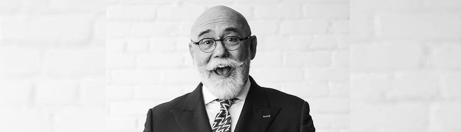 A black-and-white photo of Scott McKeen smiling in front of a white brick wall