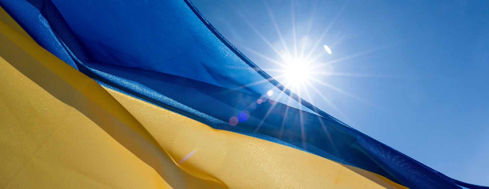 A Ukrainian flag waving in front of a bright sun and blue sky