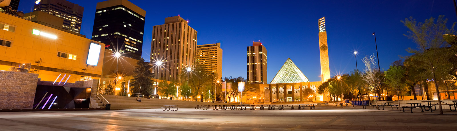 An evening photo of Edmonton's City Hall with a dark blue skyline and a fully lit square