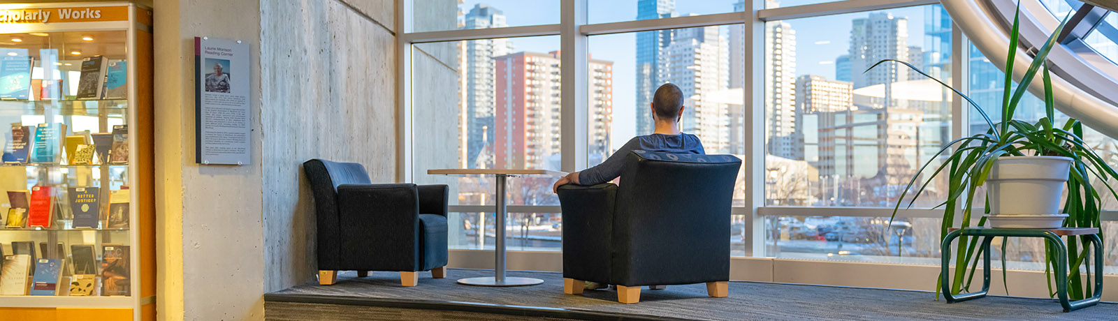 A student sits in a blue armchair looking out at the view of Edmonton's downtown from the new Laurie Morison Reading Corner.