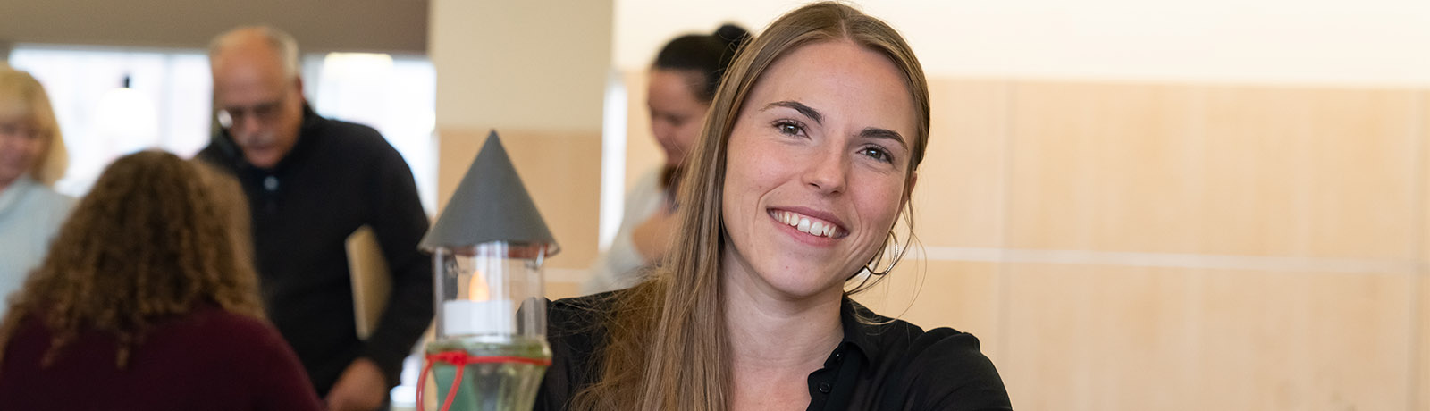 Jenna Kuruliak sits at a table with her project - a glass lighthouse on top of a cardbaord illustration of the sea along with funnels, ribbon, flowers and seashells