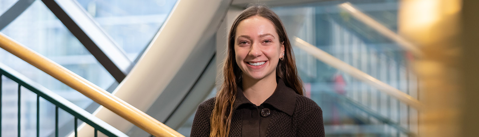 Jessalyn LeBlanc stands in front of the clock tower in the library wearing a dark jacket with big buttons and jeans.