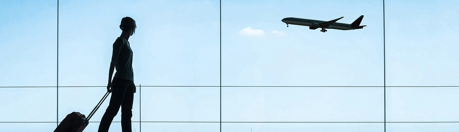 silhouette of person walking through an airport while a plane lands in the background