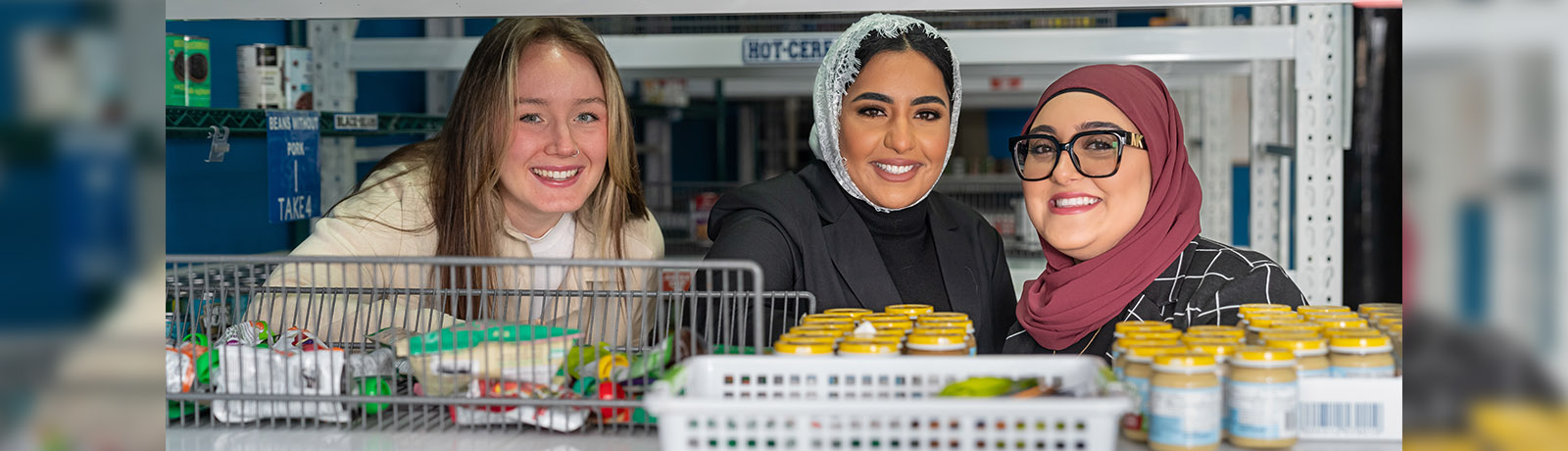 Three students stand among the shelves in the C5 Hub Pantry