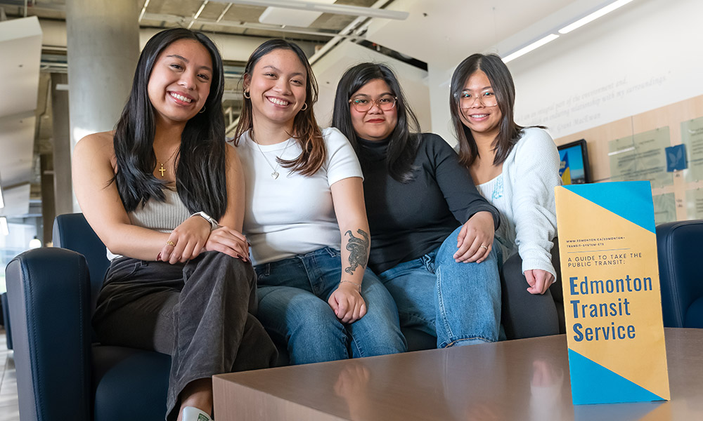 Four students sit on a sofa beside a table that holds a brochure they created 