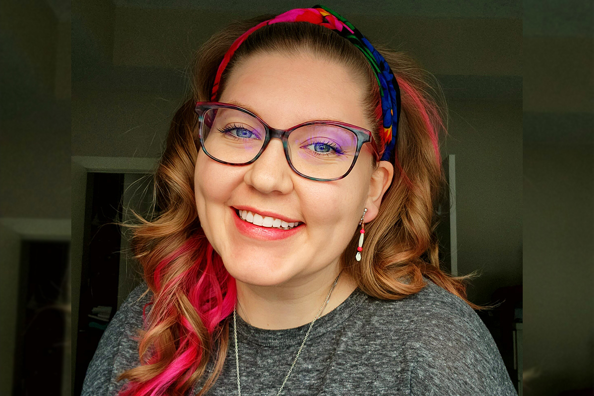 Alixaunrdia Lamothe is wearing a grey sweater and colourful headband, and is smiling at the camera