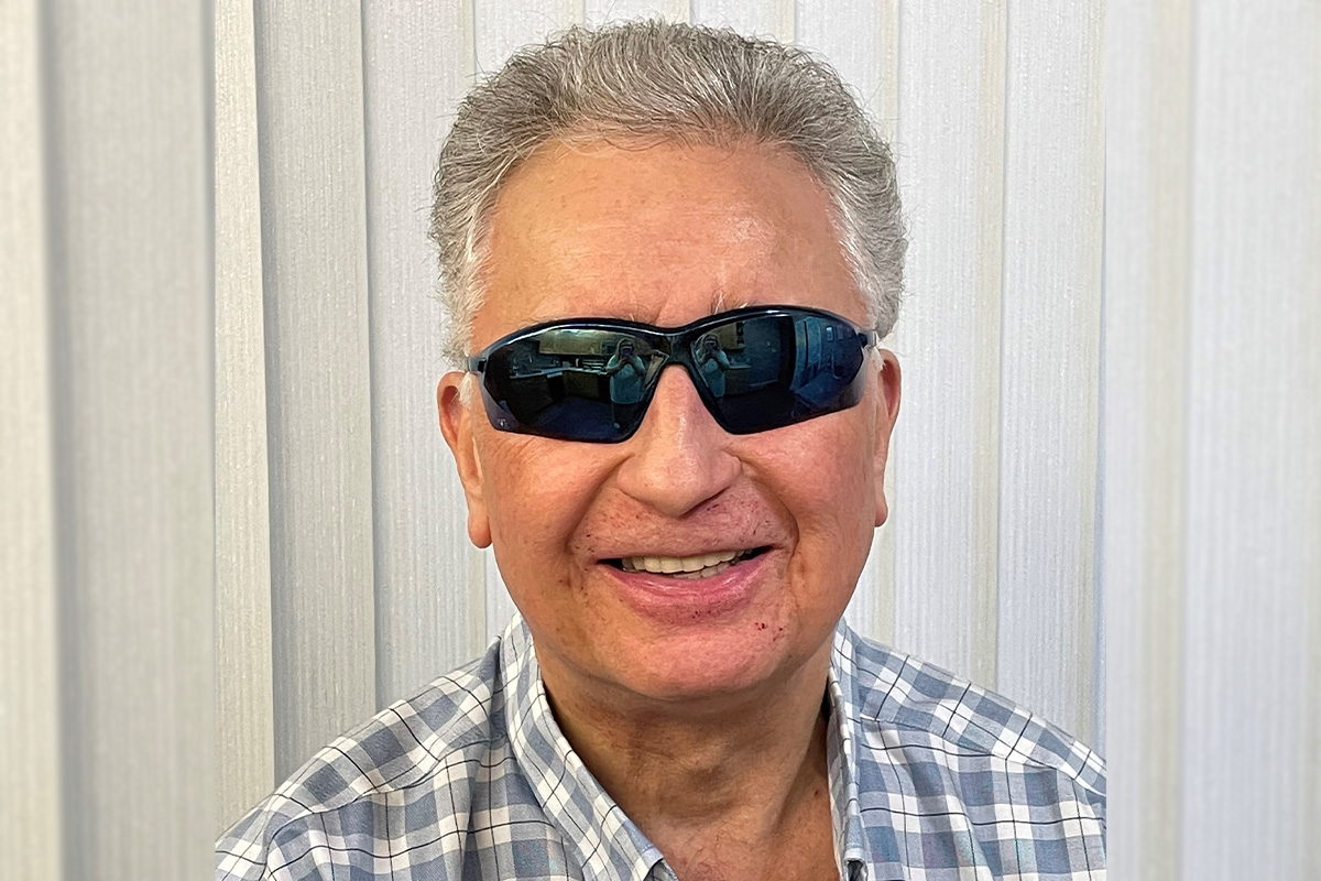 Russell Solowoniuk is smiling at the camera, wearing sunglasses and a grey and white plaid shirt