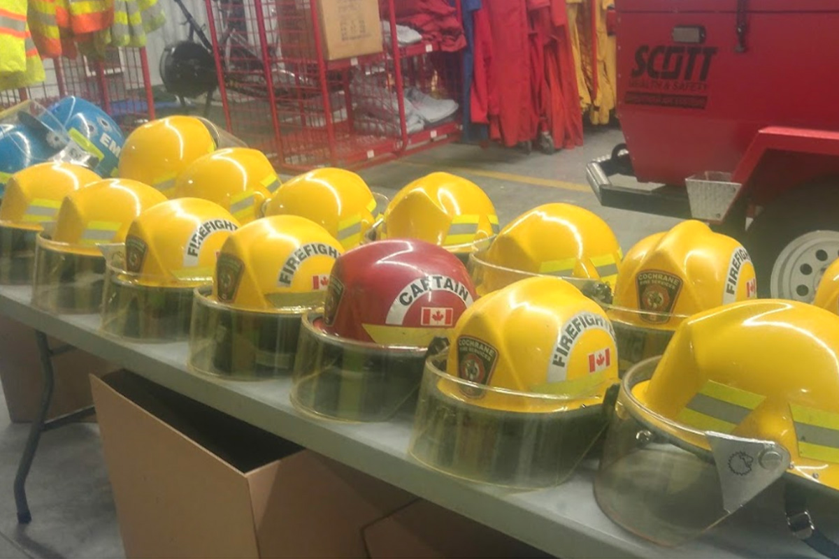 Yellow and red firefighter helmets line a folding table with a fire engine in the background