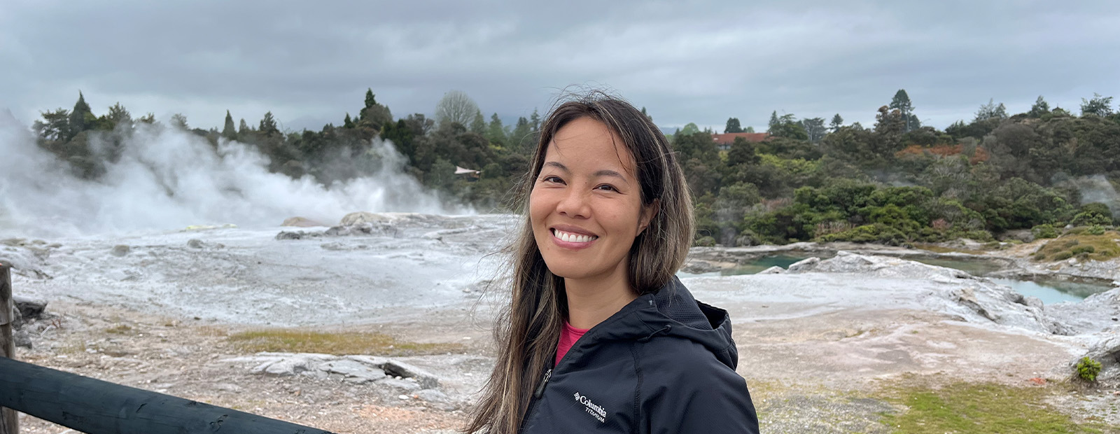 Vivian Giang wears a black windbreaker and stands in front of the ocean, where large waves are crashing against the shore