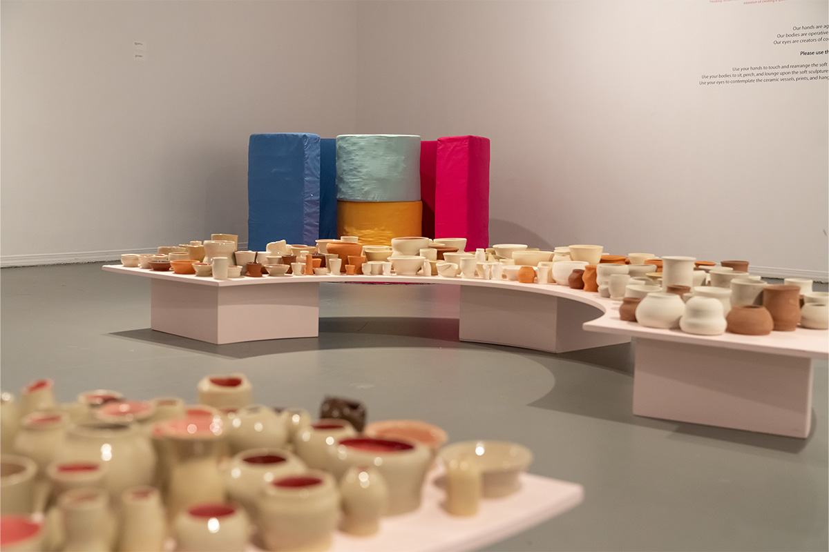Two very large semi-circle tables are covered in small ceramic vessels in varying shades of brown and white