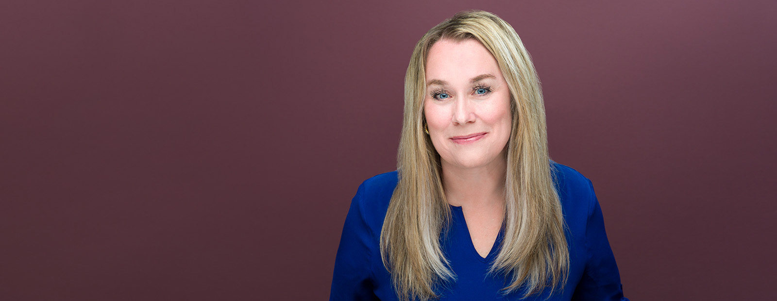 A headshot of Lara McClelland wearing a blue top in front of a maroon background