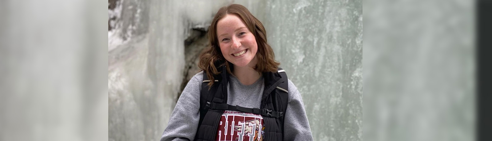 Paitlynn Hippisley stands in front of a wall of ice wearing a backpack and her Griffins sweatshirt