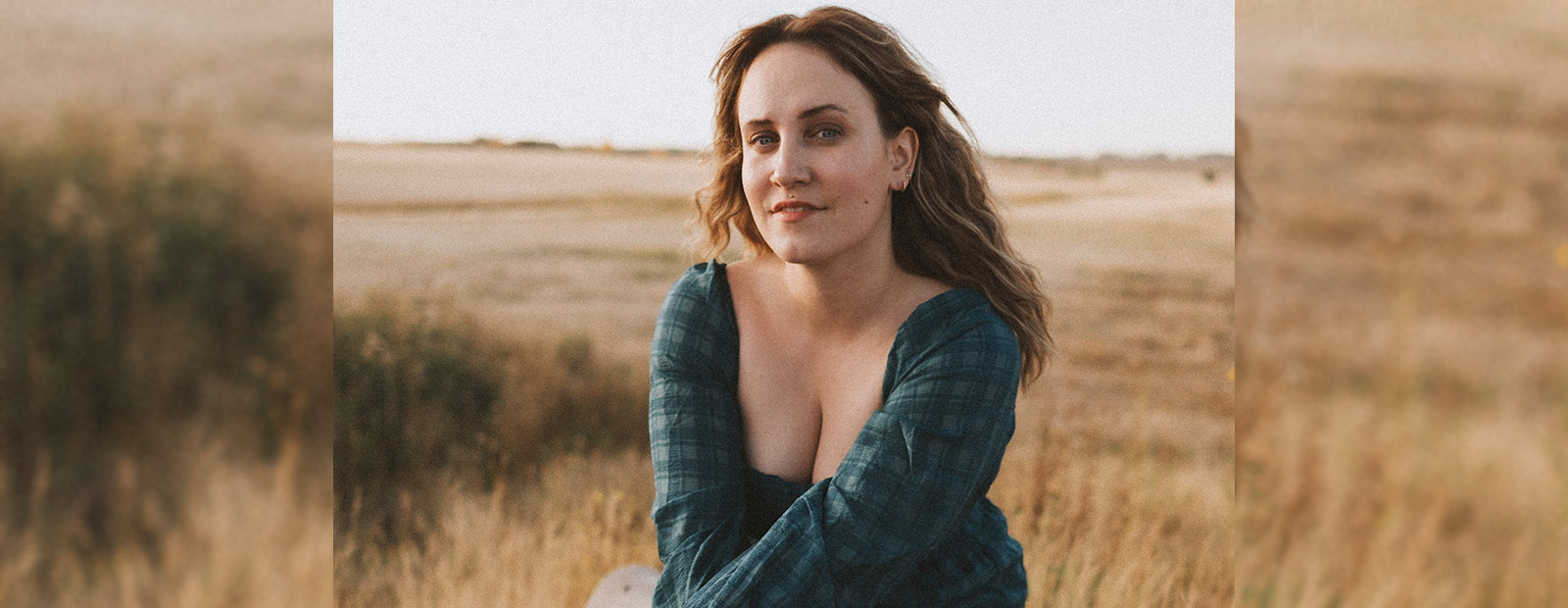 Mallory Chipman sits on a concrete barrier at the edge of a wheat field. She rests her forearms on her knees as a breeze blows hair back from her face.