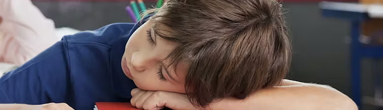 A child rests their head on top of a red book on a desk