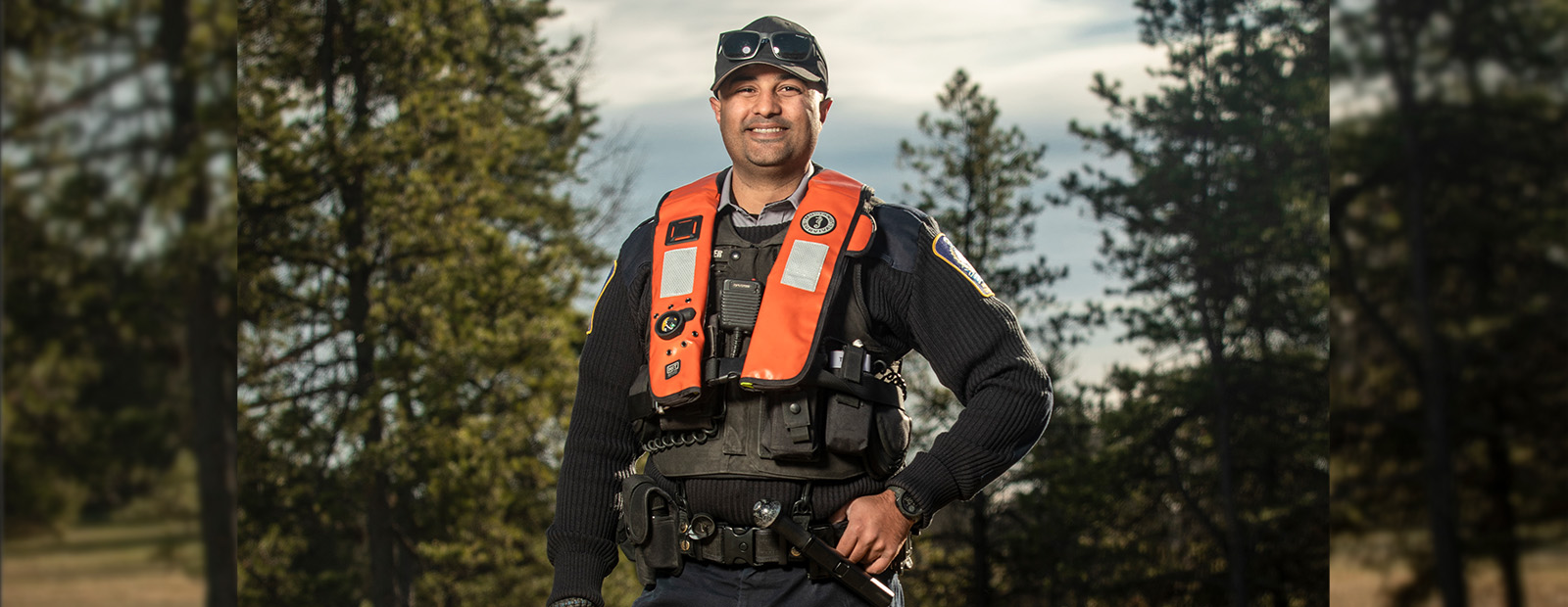 Zain Haji stands in front of a wooded area in his full park ranger uniform