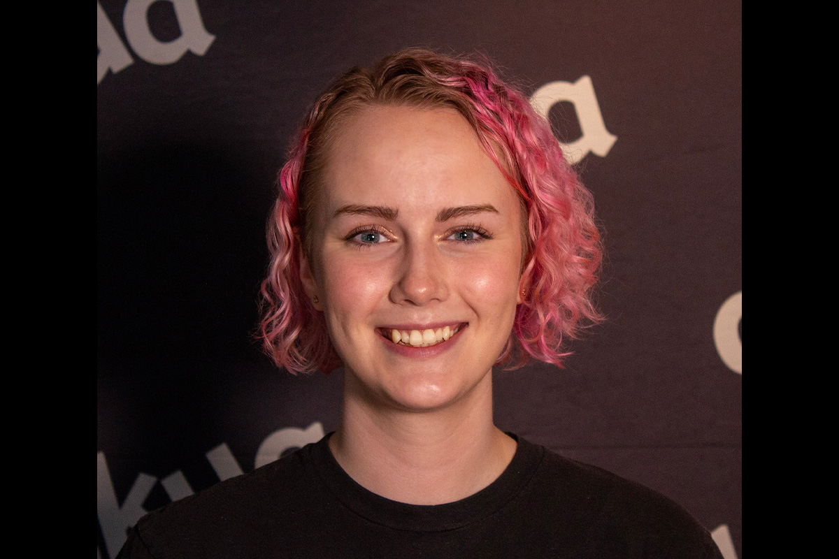 A person with pink hair smiles at the camera