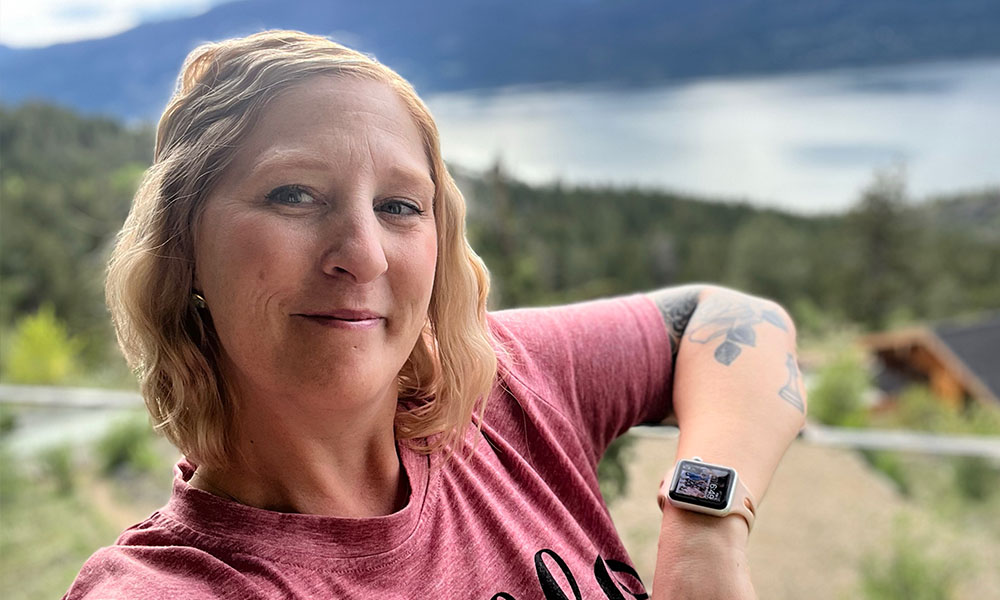 Jill leans against a railing overlooking water and mountains