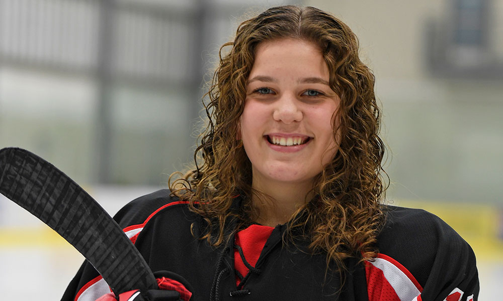 Kristina smiles while standing in her hockey uniform at the rink