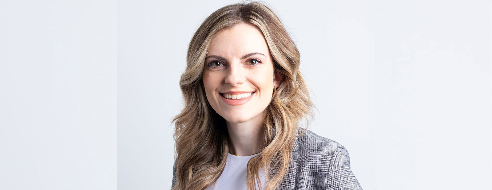 A headshot of Inez Agovic. She has long, curled blonde hair and wears a grey blazer.