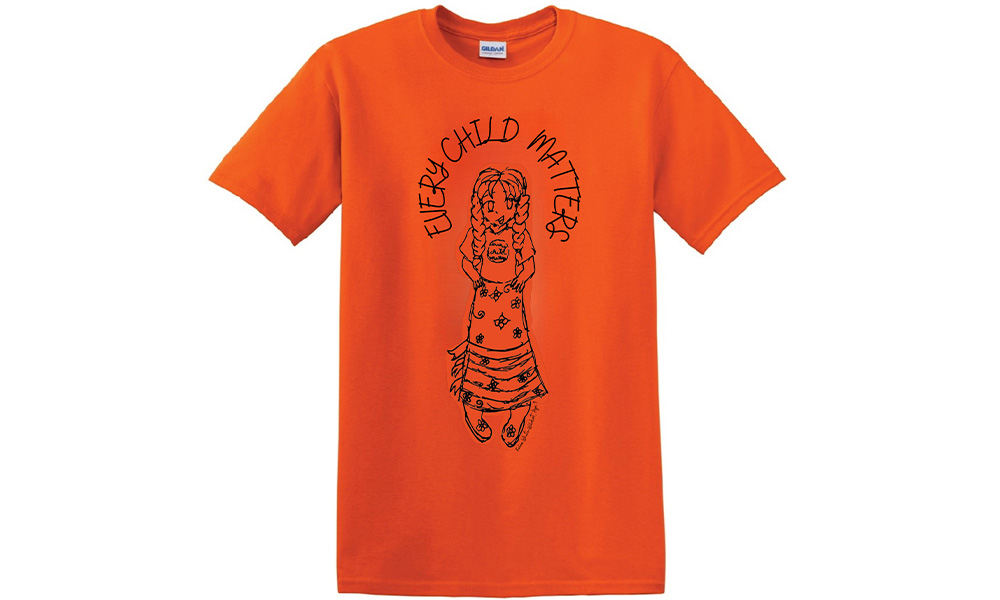 An orange tee shirt with a drawing of a girl with braids wearing a ribbon skirt