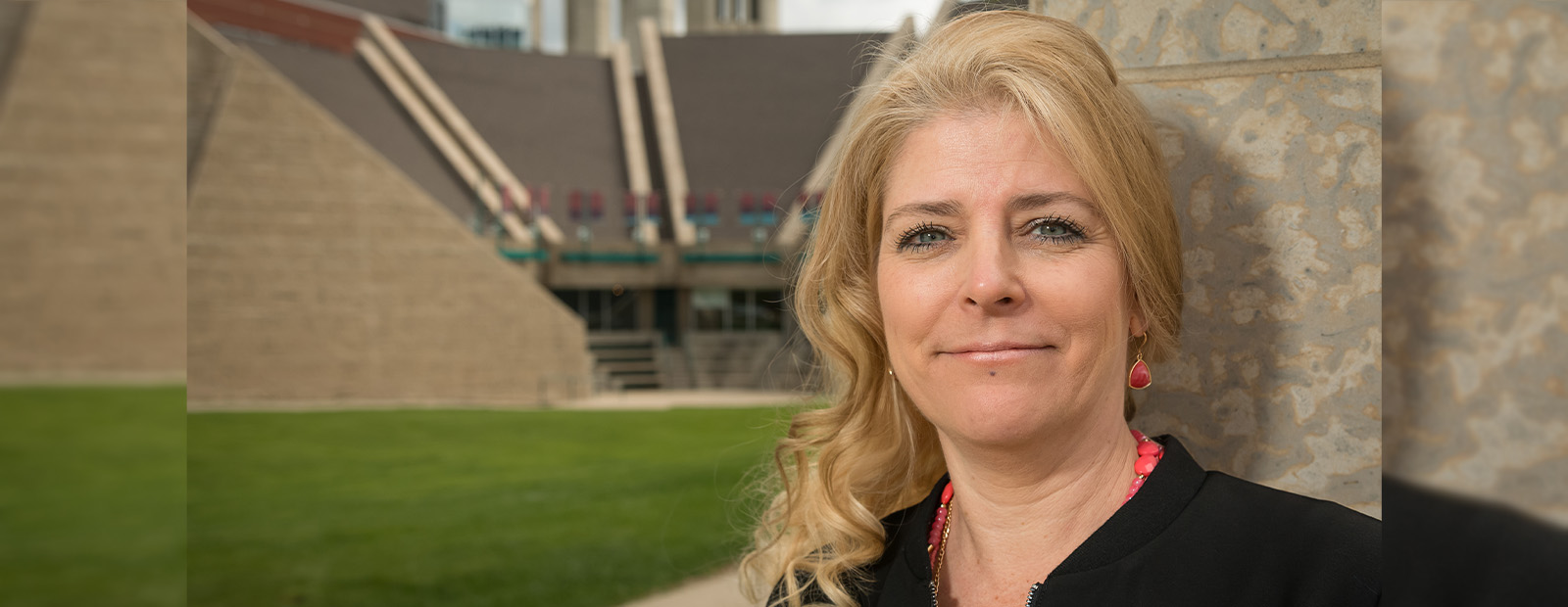 Diane Symbaluk stands in front of a stone pillar outside of Building 7 and smiles at the camera.