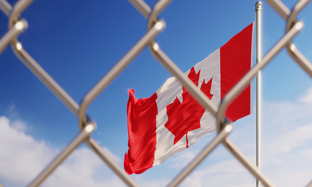 A Canadian flag flies behind a chain-link fence