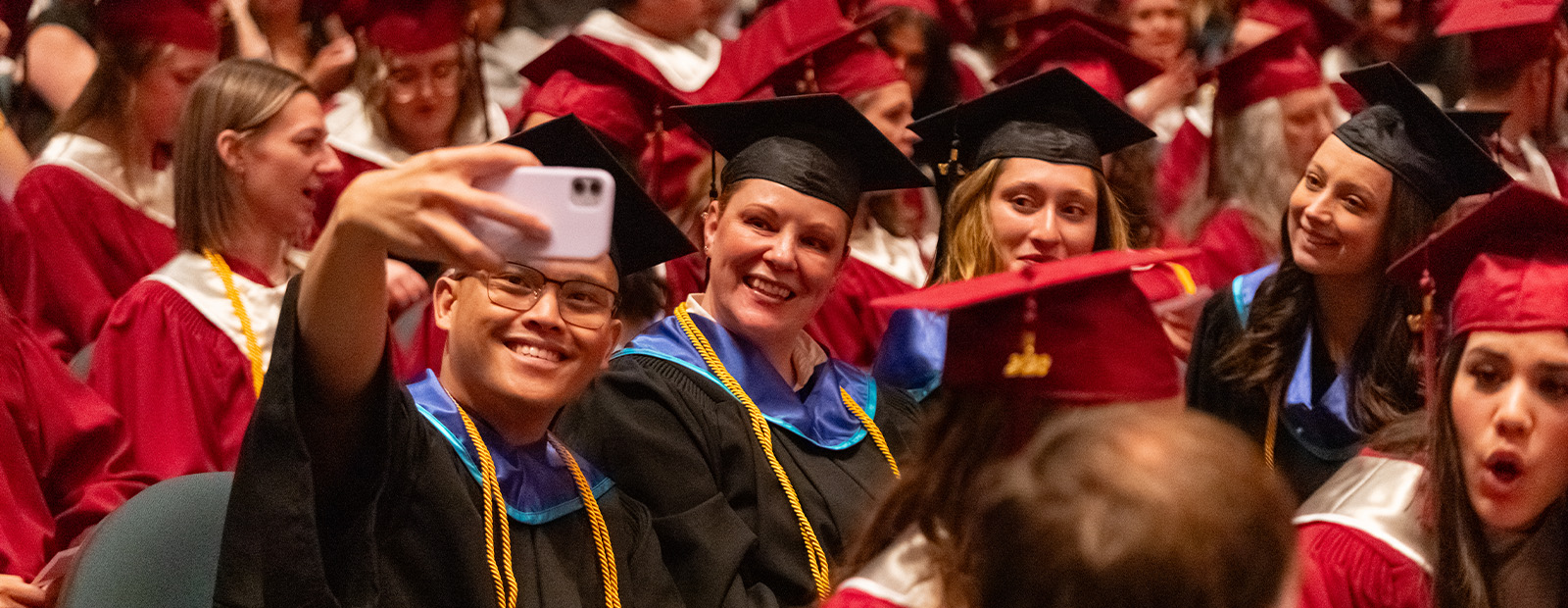 Four graduates take a selfie together among the crowd at convocation.