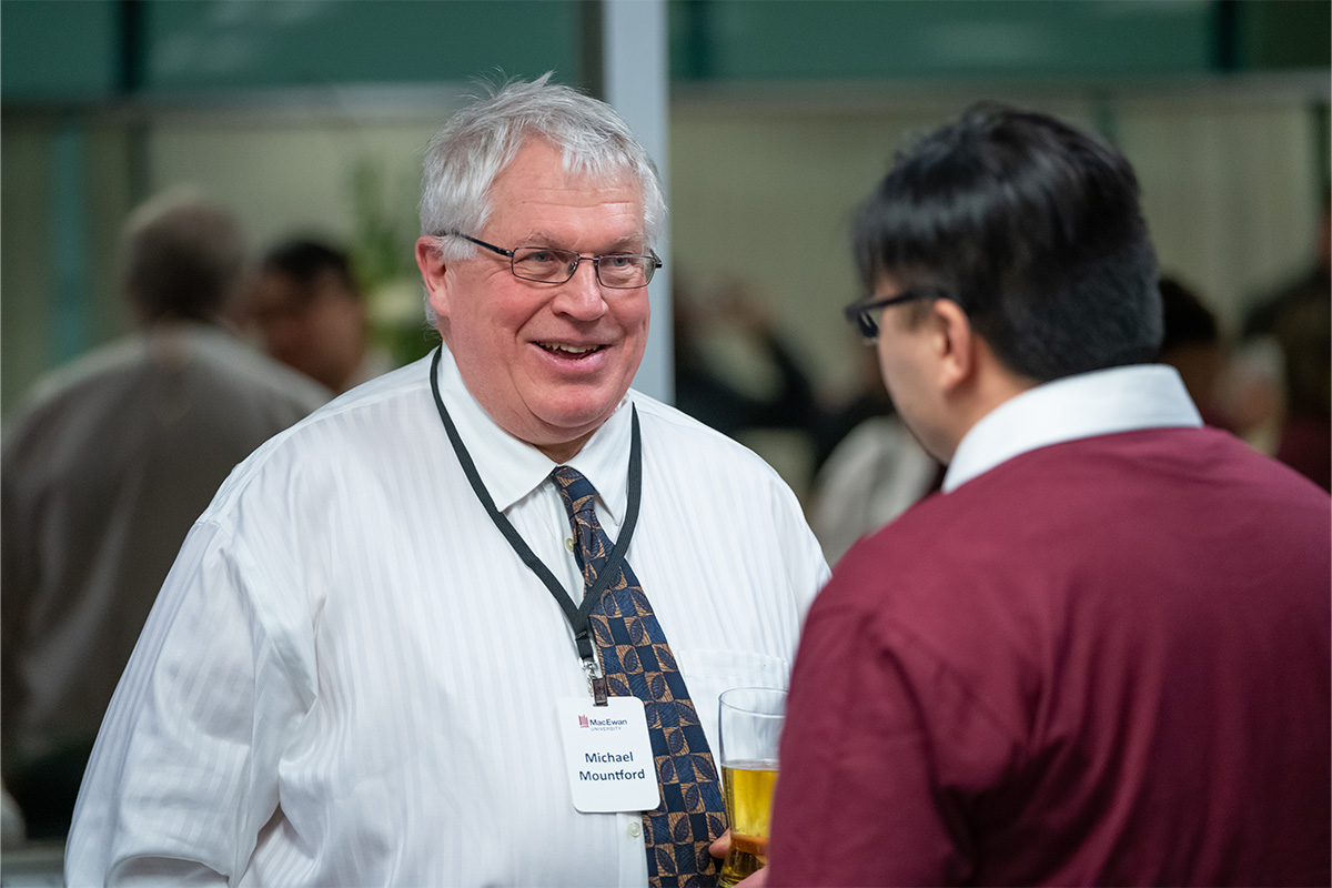 Michael Mountford wears a white button-down shirt and smiles as he speaks to someone at a donor appreciation event.