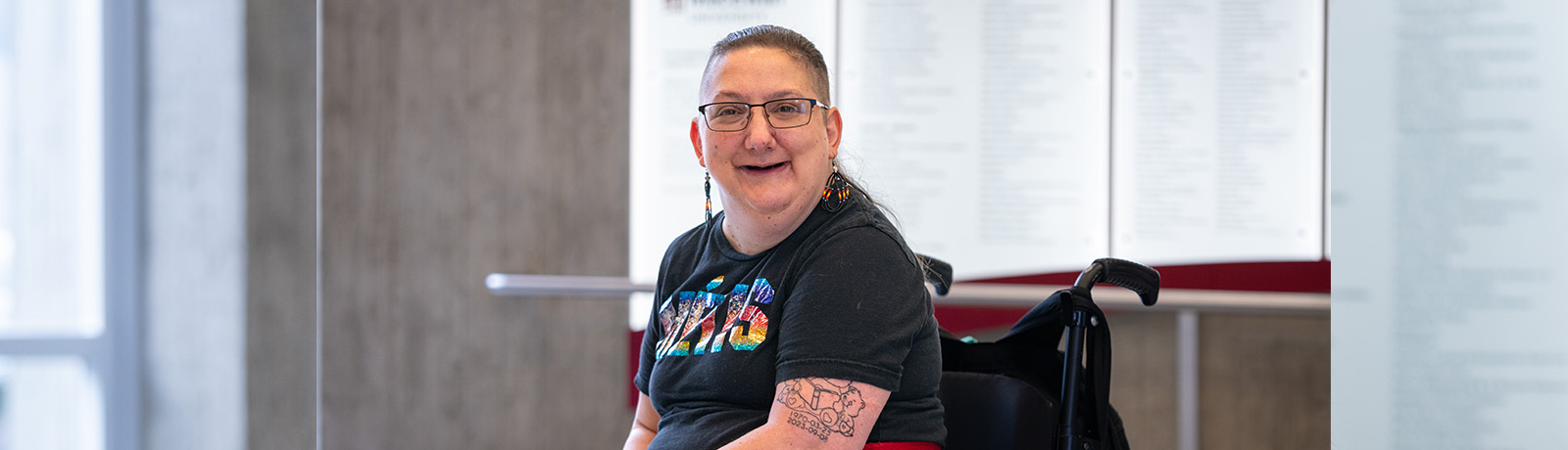Al Olsen smiles, wearing a t-shirt with the word Metis on it, spelled out in rainbow colours